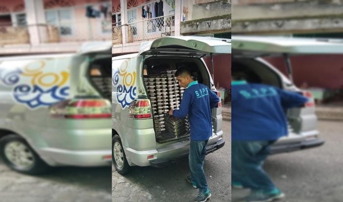 Tumpukan Kotak Makanan Siap Dibagikan, dengan Kepala Madrasah Afrinal Mengawasi